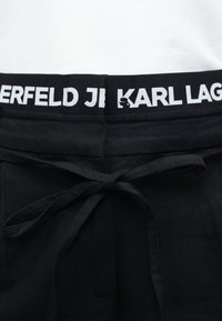 Μαύρο παντελόνι με δεμένη ζώνη υφάσματος και ζώνη μέσης με λευκό κείμενο που αναγράφει "KARL LAGERFELD".