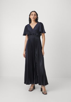 Marineblauwe maxi-jurk met plooien, korte fladdermouwen, een diepe V-hals en een geraffineerde taille detail. Gecombineerd met gestrikte haksandalen.