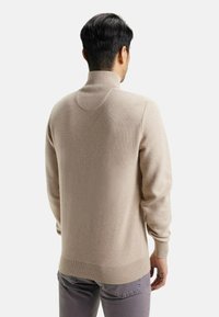 Pull en tricot beige avec un col montant, un design texturé et un ourlet côtelé. Idéal pour un look décontracté. Il dispose de manches longues et d'une coupe décontractée.