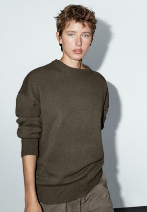 Braun gestrickter Pullover mit Rundhalsausschnitt und fallenden Schultern. Der Stoff wirkt weich mit gerippten Bündchen und Saum. Eine subtile Textur ist sichtbar.