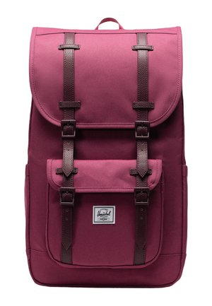 Maroon backpack made of durable fabric, featuring a flap closure, brown leather straps, front pocket, and a logo patch.