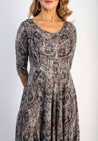 Schwarzes Kleid mit einem Paisleymuster in Weiß-, Rot- und Beigetönen. Hat einen runden Ausschnitt und dreiviertel Ärmel, gefertigt aus einem glatten Stoff.