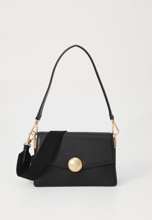 Black leather handbag with a gold circular clasp, featuring a detachable black fabric strap and a structured design with sharp edges.
