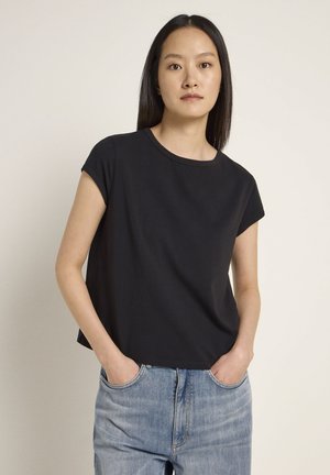 Schwarzes kurzärmeliges T-Shirt mit Rundhals, aus weichem Material gefertigt. Kombiniert mit hellblauen, hochgeschnittenen Jeans, die Hände in den Taschen.