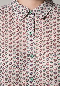 Camicia button-up di colore chiaro con un motivo floreale, dotata di bottoni verdi, colletto a punta e una texture liscia.