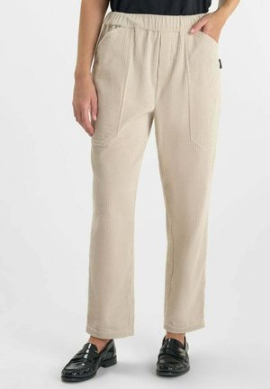 Pantalons en velours côtelé beige avec une coupe décontractée, taille élastique et poches latérales, associés à des mocassins noirs.