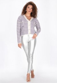 Lila és fehér tweed kardigán V-nyakkal, gombos záródással és hosszú ujjakkal, fényes ezüst domború nadrággal párosítva.