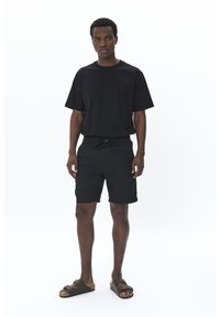 Black short-sleeve T-shirt, black elastic-waist shorts, and brown sandals with straps. Plain design, lightweight fabric, relaxed fit.