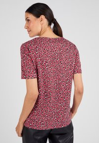 Camisa de manga corta en rojo con estampado de leopardo en negro y blanco. Tejido ligero, cuello redondo, corte relajado y textura suave.