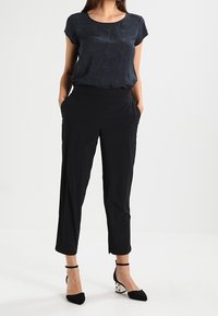 Černé zkrácené kalhoty spárované s námořnickým topem s krátkým rukávem, který má jemný vzor. Modelka má na sobě černobílé lodičky se špičatou špičkou.