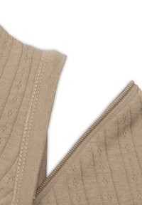 Beige gebreide stof met een geribbelde textuur en kleine decoratieve gaatjes. Heeft een gladde rand en een rits aan één zijde.