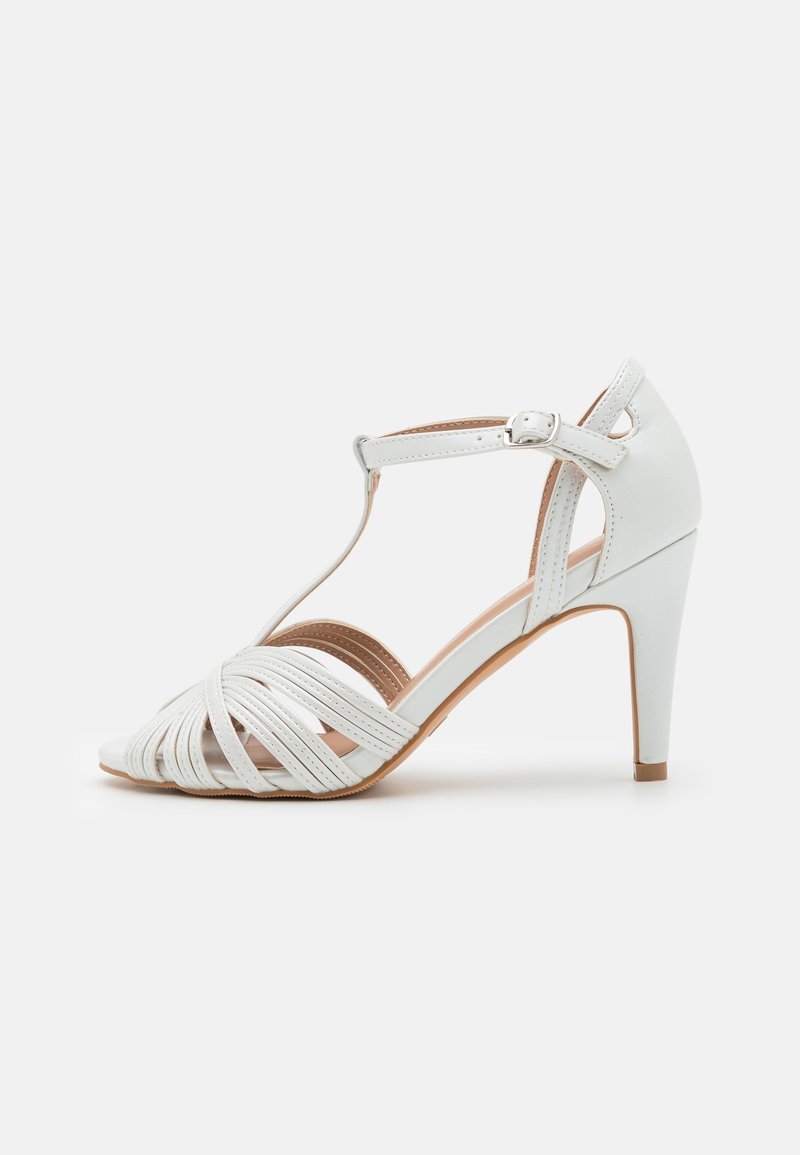 Sandale blanche à talons hauts avec bride en T, fermeture à boucle et lanières avant en cuir tressé, vue de profil sur un fond uni.