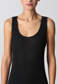 Donna che indossa un top nero senza maniche con scollatura a barca, visibile dal collo alla vita, con pelle chiara e braccia di lunghezza fino alle spalle esposte.