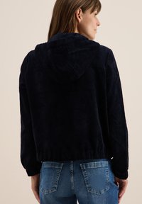 Merin vaalean sininen corduroy-takki hupparilla, jossa on ribbauspinta ja joustavat hihansuut. Yhdistetty farkkuihin, mikä tuo esiin rentoa ja istuvaa muotoilua.