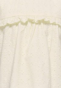 Weißes Baumwollkleid mit gestickten Blumenmustern, einem gerafften Ausschnitt und einem schlichten Rock, der die Textur und visuelle Details unterstreicht.