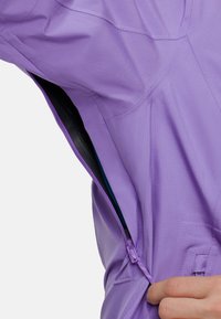 Chaqueta de color púrpura claro con apertura con cremallera, diseño elegante y tejido texturizado. Capa interior visible en azul contrastante.