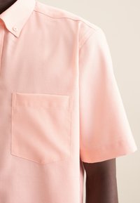 Camicia a maniche corte, con colletto, in tessuto pesco chiaro con un motivo testurizzato e una tasca sul lato sinistro del petto. Cuciture pulite e vestibilità classica.