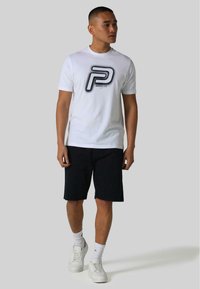 White short-sleeve t-shirt with a large black "P" logo on the front, paired with black shorts and white sneakers. Smooth fabric texture.
