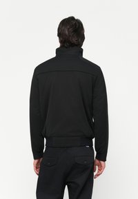 Black pullover jacket with a high collar, featuring a smooth, matte fabric, ribbed cuffs, and waistband, and a plain back design.