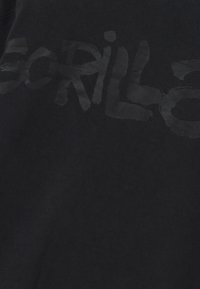 Zwarte katoenen T-shirt met grote, vervaagde zwarte tekst die "GORILLA" op de voorkant spelt. De stof lijkt glad met een lichte textuur.