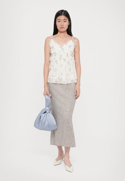 Weiße Blumen-Camisole mit Rüschensaum und dünnen Trägern, kombiniert mit einem strukturierten grauen Midirock und einer hellblauen Tasche, ergänzt durch spitze weiße Mules.