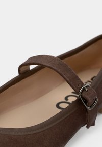 Pruun seemisnahast Mary Jane stiilis king hõbedase pandlaga rihmaga ja beež sisetald osaliselt nähtava musta tekstiga.