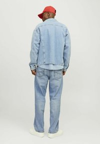 Lichtblauwe denimjack en -broek, rode pet, met een ontspannen pasvorm. Opvallende stikdetails en een omgeslagen kraag. Witte sneakers.