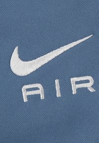 Nike Air-logoet i hvid broderi på et struktureret himmelblåt stof, med et karakteristisk swoosh og fed skrift.