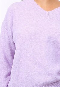 Pull lilas en V avec un tricot doux et texturé ; présente des manches amples et des bords côtelés au niveau du col et de l'ourlet.