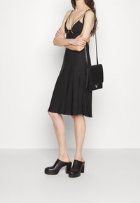 Černé bezramínkové šaty s rozšířeným lemem, vyrobené z hladké látky. V kombinaci s masivními černými dřeváky a malou černou kabelkou na kříž.