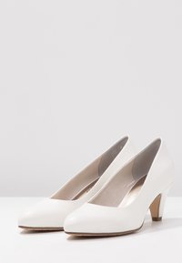 Weiße Pumps mit hohen Absätzen, glattem, glänzendem Finish, spitz zulaufender Spitze und einem mittelhohen, gestapelten Absatz. Das Innenfutter ist weich gepolstert.