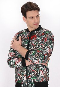 Giacca bomber con stampa multicolore di foglie e uccelli, dotata di colletto e polsini neri, chiusura con zip e una texture del tessuto liscia.