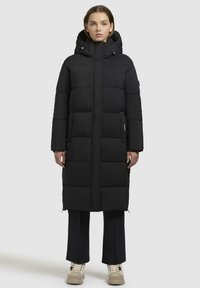 Sort polstret lang jakke med hætte, med en hel længde lynlås og to sidelommer. Stoffet har en glat tekstur. Casual pasform.