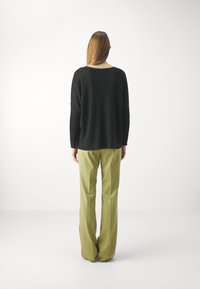 Svart stickad tröja med avslappnad passform och vid halsringning, parat med ljusgrön, skräddarsydd byxa med vida ben. Slät struktur genom hela.