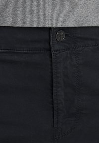 Schwarze Hose aus texturiertem Stoff, mit Knopfverschluss und genähten Details. Das Kleidungsstück hat eine glatte Oberfläche und klassische Designelemente.