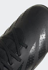 Zapatilla deportiva negra con parte superior sintética texturizada, que presenta cordones negros y acentos plateados reflectantes en un diseño aerodinámico.
