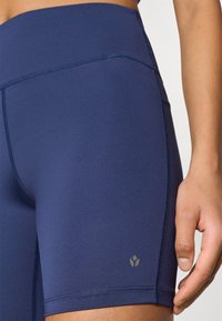 Tmavomodré športové šortky z hladkej, elastickej látky. Majú ploché švy, vysoký pás a malý logotyp na dolnej strane.