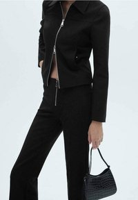 Veste noire ajustée zippée avec col, associée à un pantalon slim assorti et un petit sac à main en croco noir estampé.