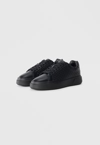 Black sneakers featuring a textured upper with a diamond pattern, sleek design, rounded toe, and thick rubber sole.