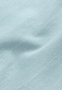 Tissu bleu clair avec une fine texture tissée et des lignes diagonales subtiles créant des plis et des ombres douces.
