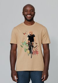 Beige t-shirt met korte mouwen met een afbeelding van een tijger op een fiets, omringd door tropische planten en bloemen, in levendige kleuren.