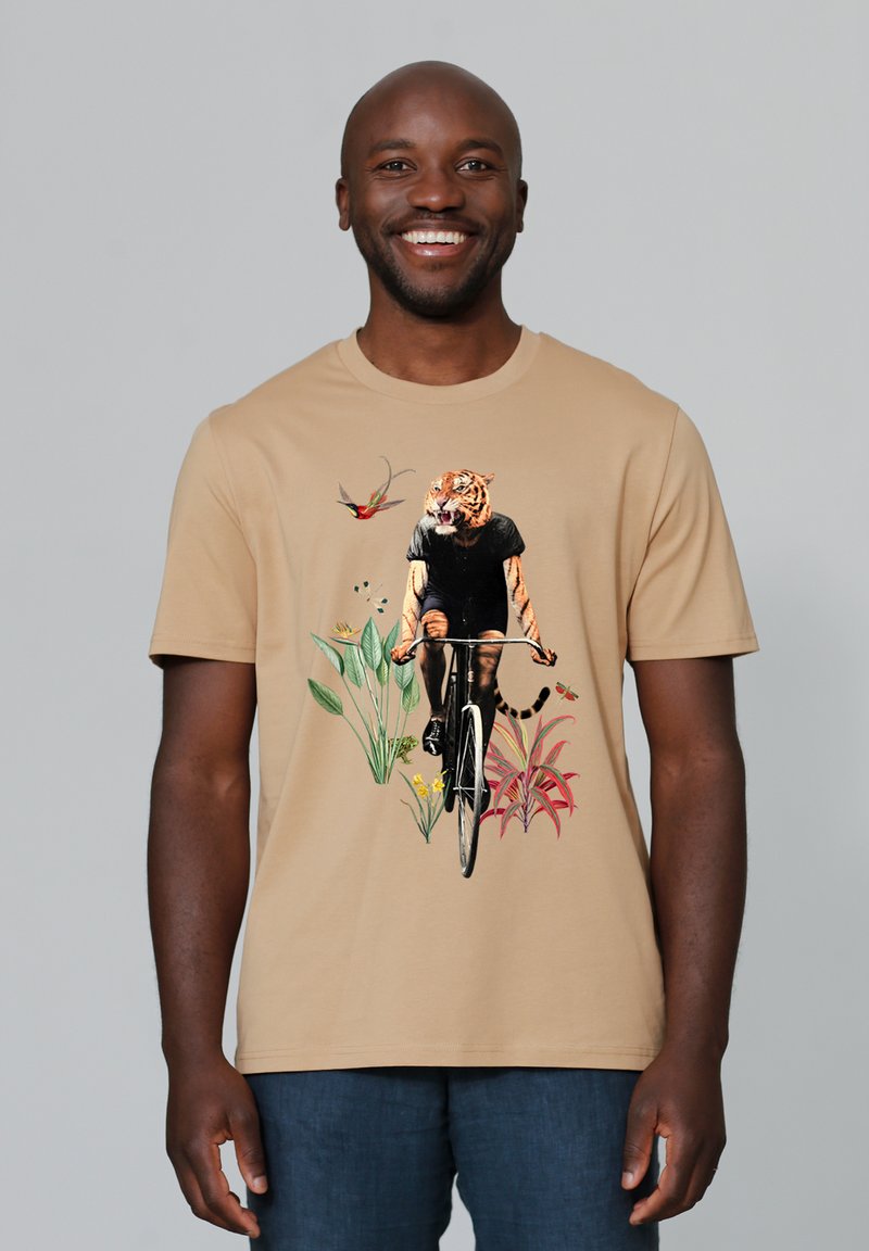 Beige t-shirt met korte mouwen met een afbeelding van een tijger op een fiets, omringd door tropische planten en bloemen, in levendige kleuren.