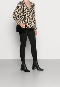 Blouse à imprimé léopard avec manches à volants, associée à un jean skinny noir et des bottines noires. La blouse présente un col en V.