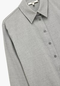 Grå skjorte med knaplukning og klassisk krave, lavet af struktureret stof, med knapper ned langs fronten og lange ærmer.