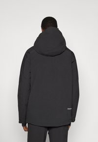 Schwarze Kapuzenjacke mit einer glatten, matten Textur und einem längeren hinteren Saum. Logo-Detail nahe dem unteren Saum auf der linken Seite.