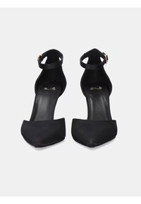 Zapatos de tacón alto negros con punta afilada, hechos de material liso. Cuentan con una correa en el tobillo con una hebilla metálica. Suela plana.