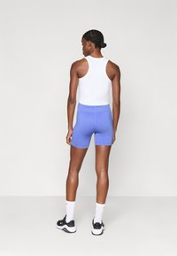 Nike Pro αμάνικο λευκό μπλουζάκι, σε συνδυασμό με μπλε σορτσάκι. Το σορτσάκι διαθέτει ψηλό λάστιχο με κείμενο "NIKE PRO" και απαλή υφή. Μαύρα αθλητικά παπούτσια και λευκές κάλτσες ολοκληρώνουν το σύνολο.