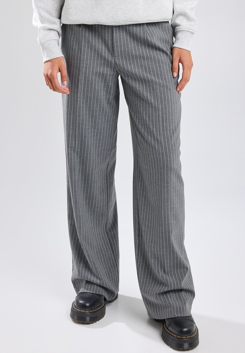 Pantalons larges à rayures verticales grises en tissu doux. La ceinture est plate, avec des lignes verticales subtiles et un matériel minimalement visible.