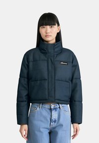 Giacca puffer trapuntata blu navy con alto colletto, due tasche frontali e patch con logo. Presenta una finitura testurizzata e una silhoutte cropped.