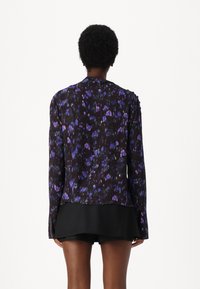 Long-sleeve blouse in sheer black fabric with purple and blue floral patterns. Hem is slightly longer at the back, featuring subtle shoulder detailing.